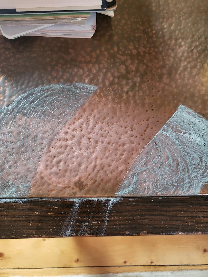 Wipping copper table clean to reveal all grime gone.